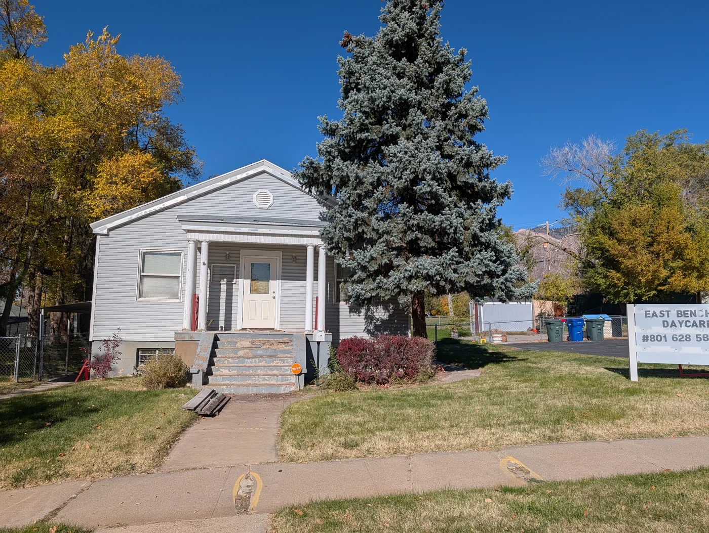 Front exterior of Ogden Little Explorers daycare building with mature pine tree and green lawn
