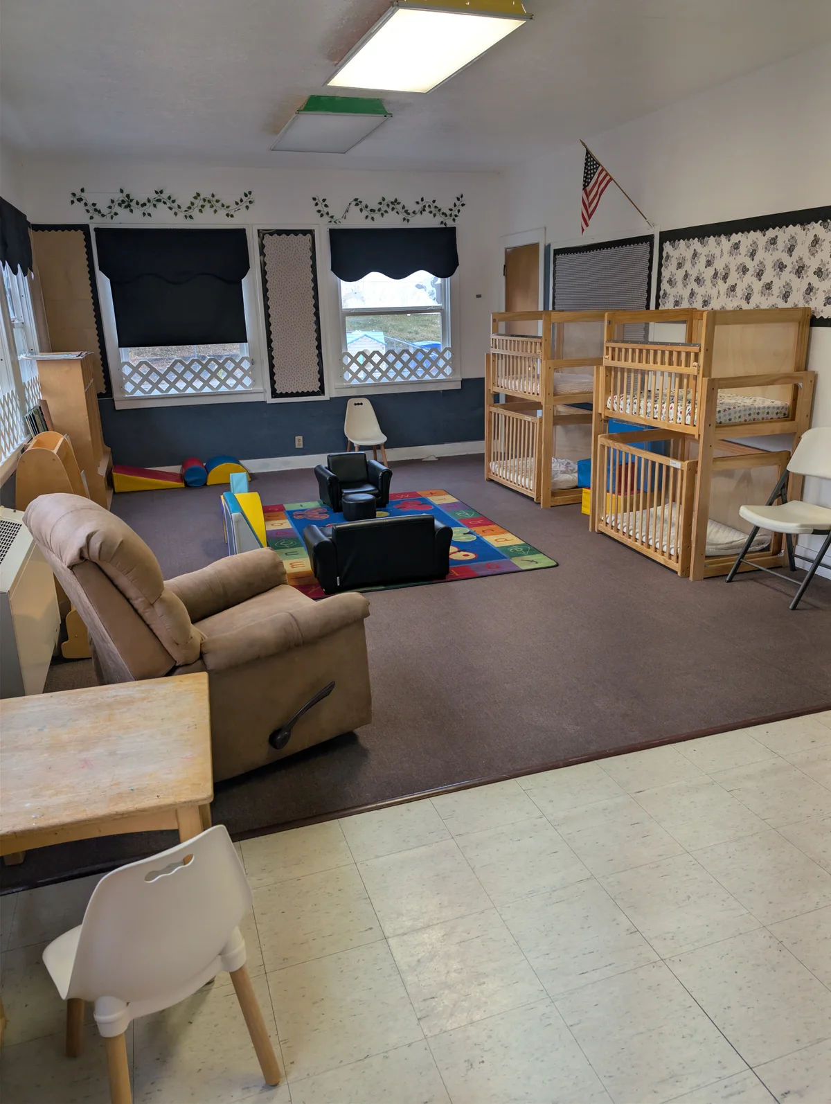 Cozy infant discovery room with solid wooden cribs, play mat and rocker